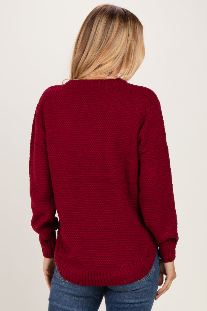 woman wearing a burgundy chunky knit sweater with a round neckline and long sleeves, seen from the back