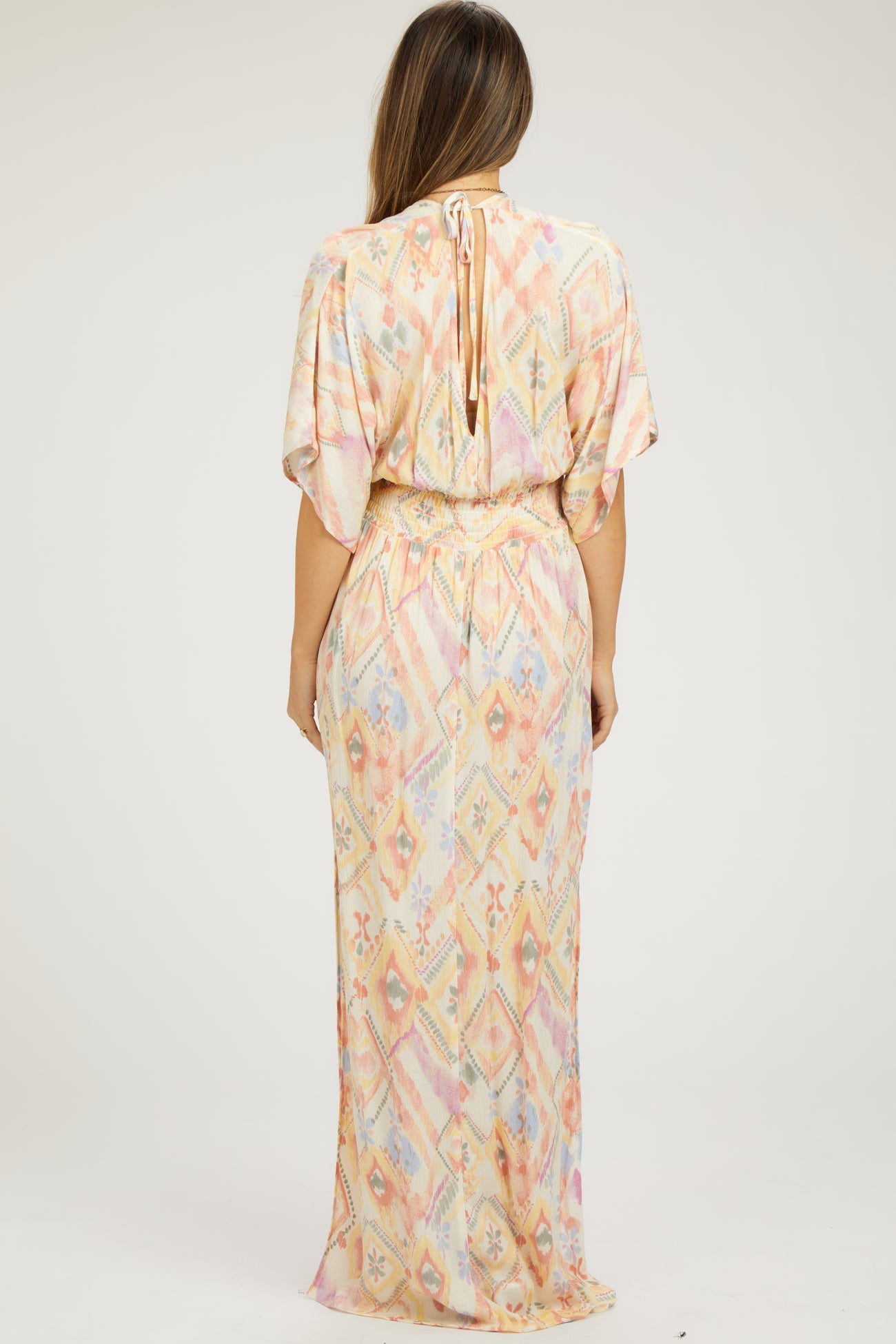 woman wearing a pastel patterned maternity maxi dress with short sleeves and a tie at the neck.