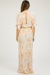 woman wearing a pastel patterned maternity maxi dress with short sleeves and a tie at the neck.