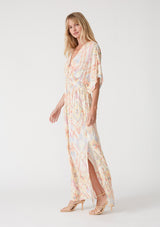 woman wearing a pastel-colored maxi dress with a geometric pattern and side slits, standing in profile with one hand on her hip