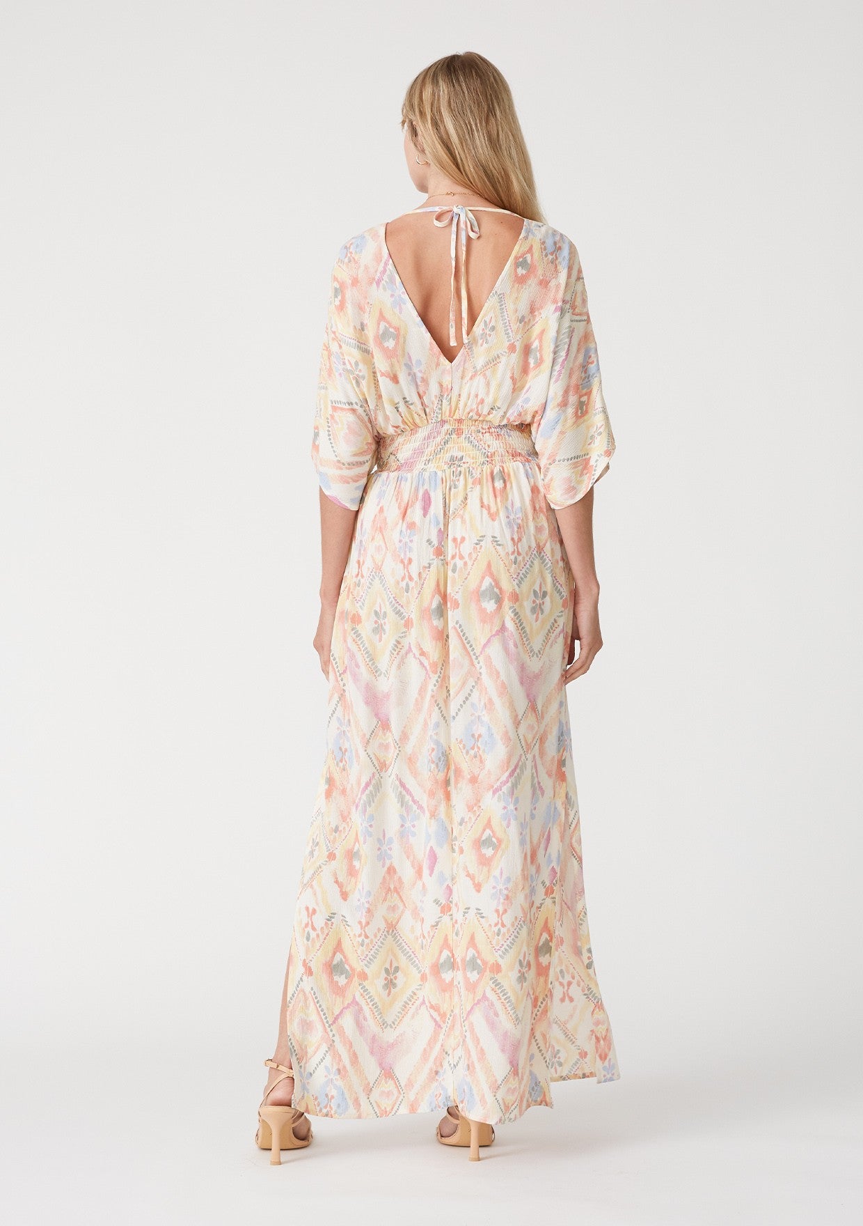 woman wearing a colorful patterned maxi dress with a tie back and side slits, showcased from the back