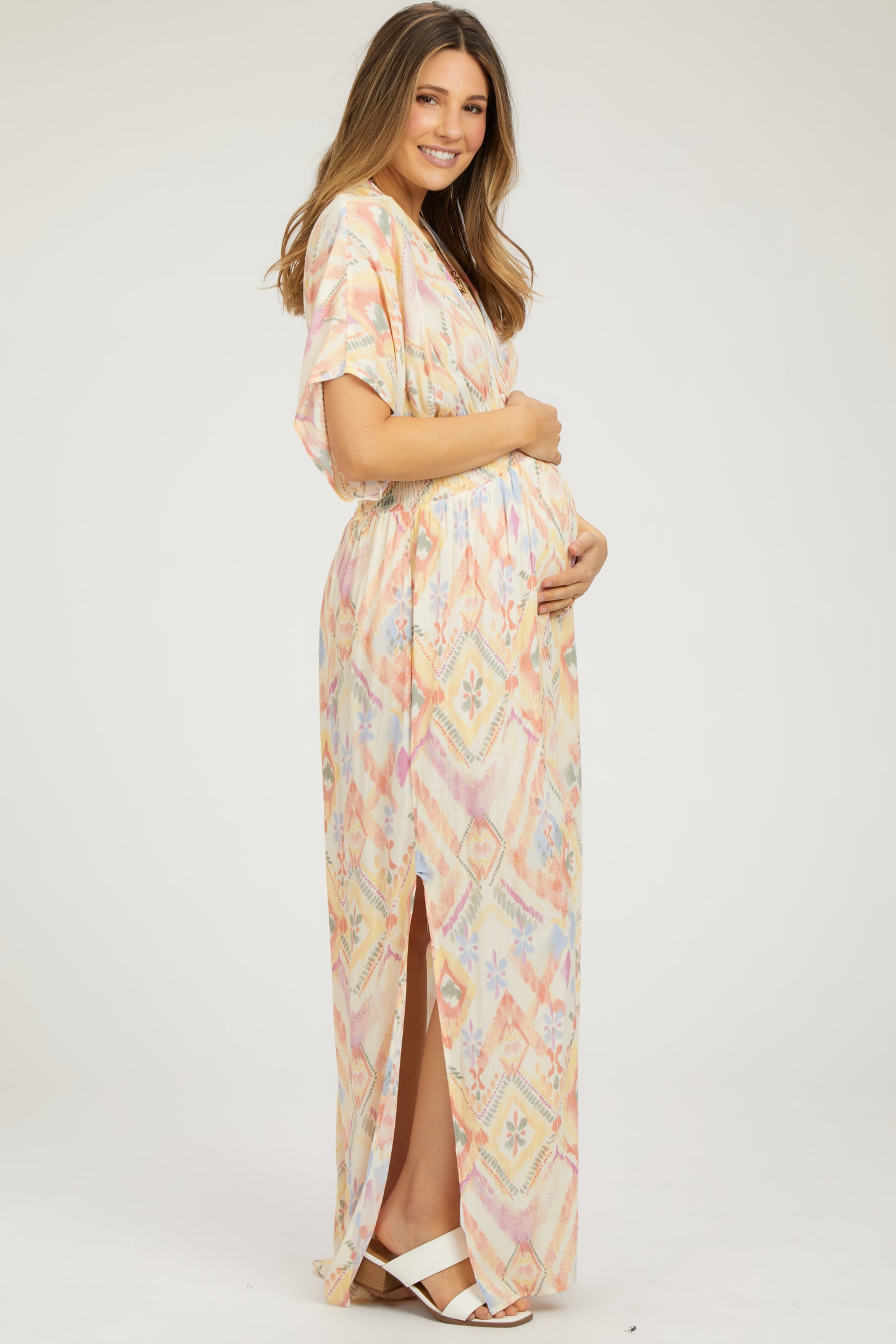 woman wearing a colorful patterned maternity maxi dress with a side slit, holding her baby bump