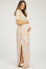 woman wearing a colorful patterned maternity maxi dress with a side slit, holding her baby bump