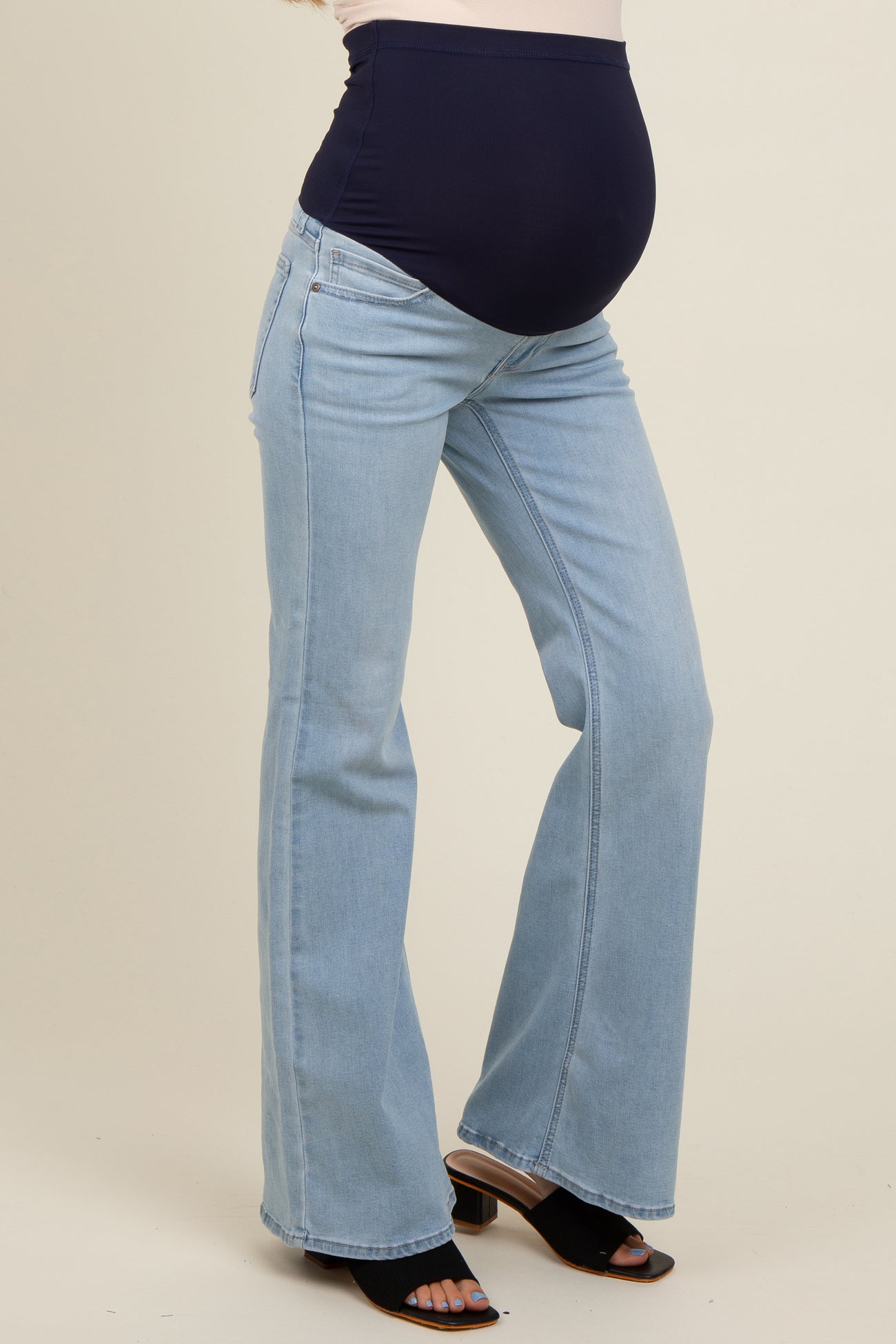 woman wearing light blue maternity flared jeans with a black over-the-bump waistband and visible baby bump