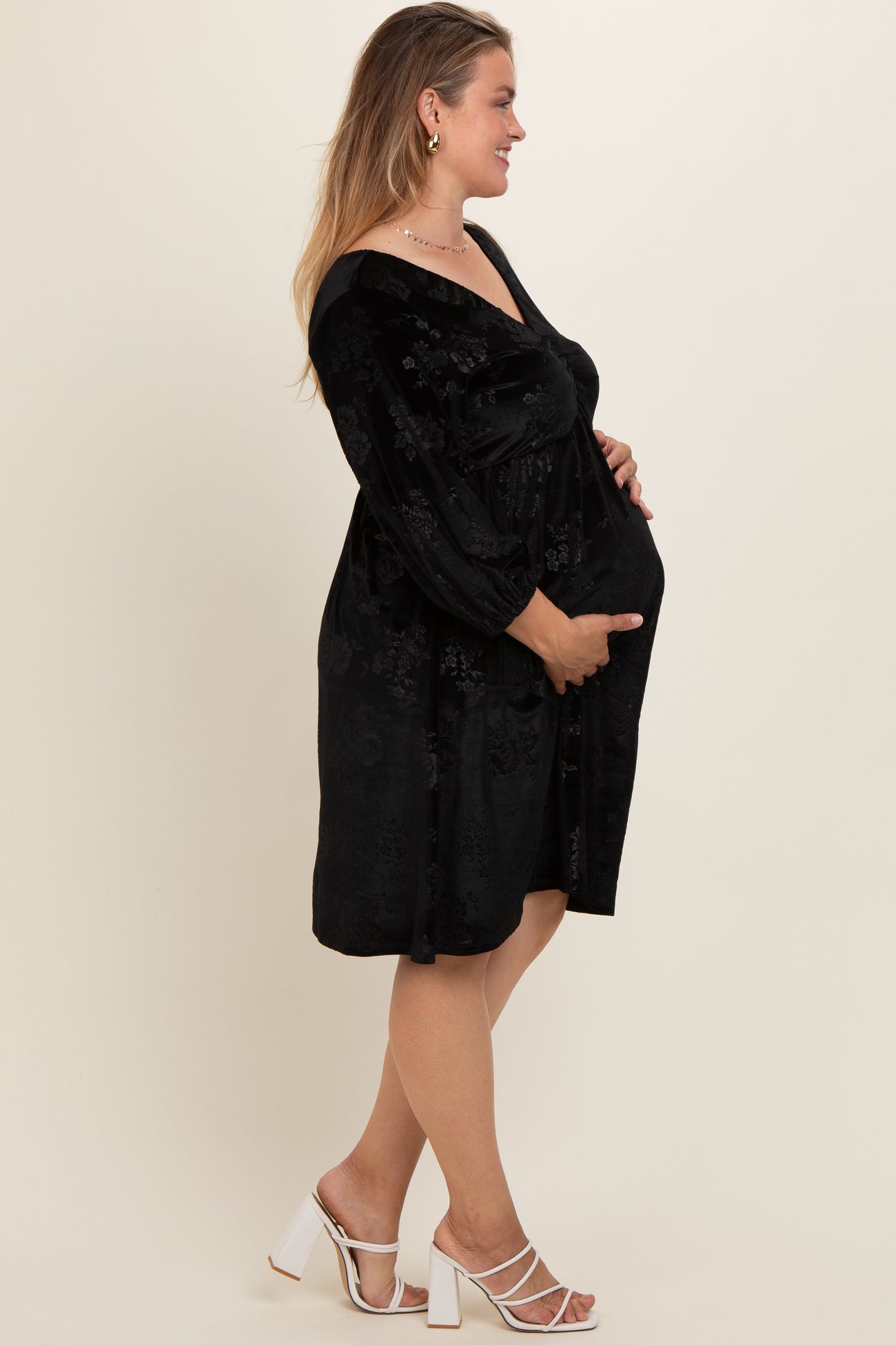 woman wearing a black floral maternity dress, holding her baby bump while standing sideways
