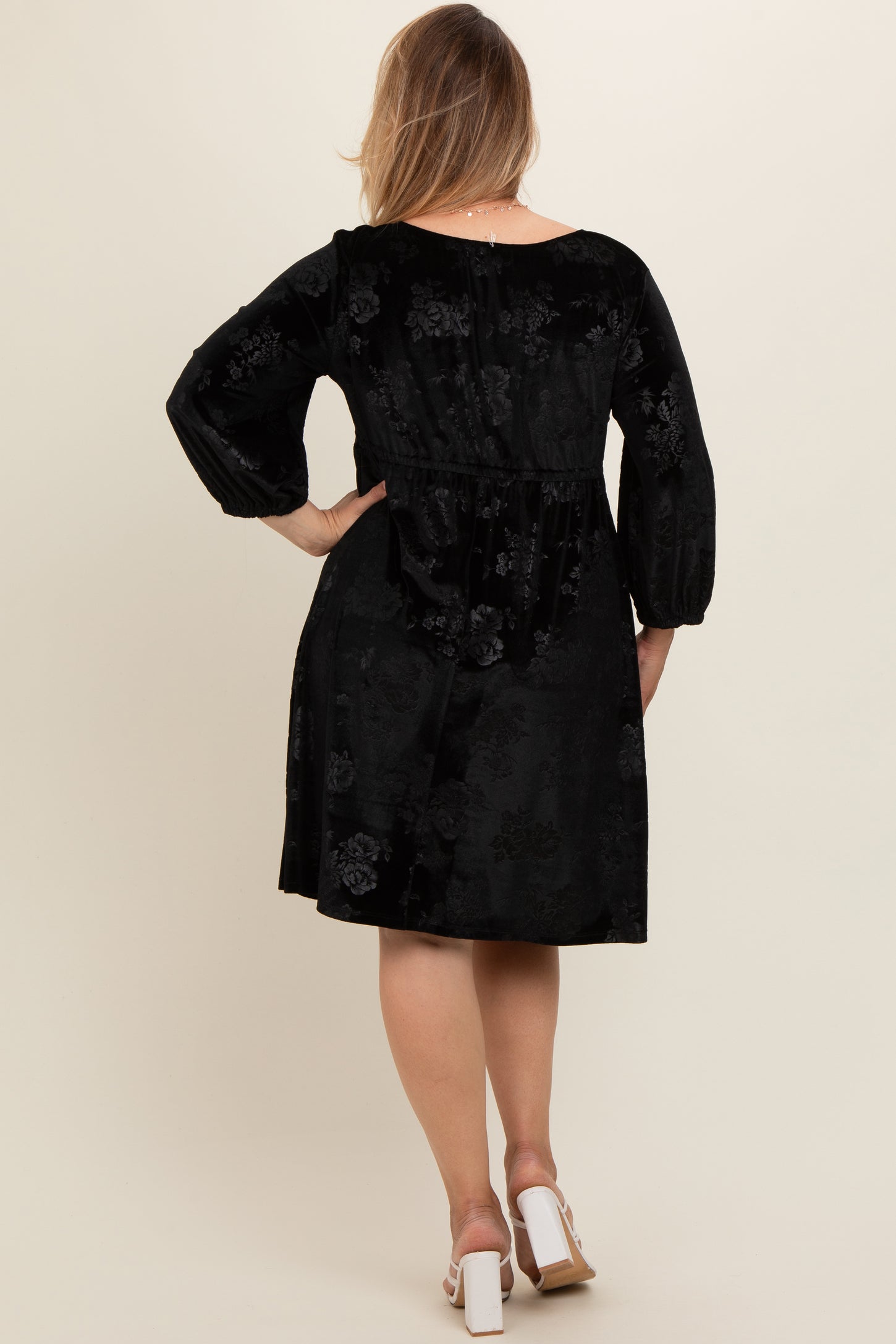 woman wearing a black velvet maternity plus dress with floral pattern and puff sleeves, showing the back view
