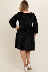 woman wearing a black velvet maternity plus dress with floral pattern and puff sleeves, showing the back view