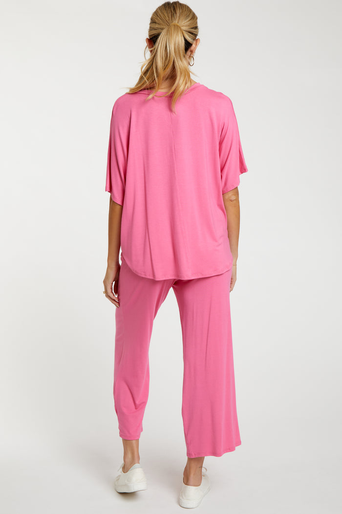 woman wearing a pink maternity loungewear set consisting of a loose top and cropped pants, showing her back