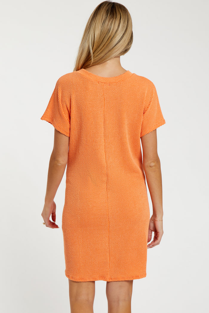 woman wearing an orange short sleeve maternity dress, showing a relaxed fit and ribbed texture from the back