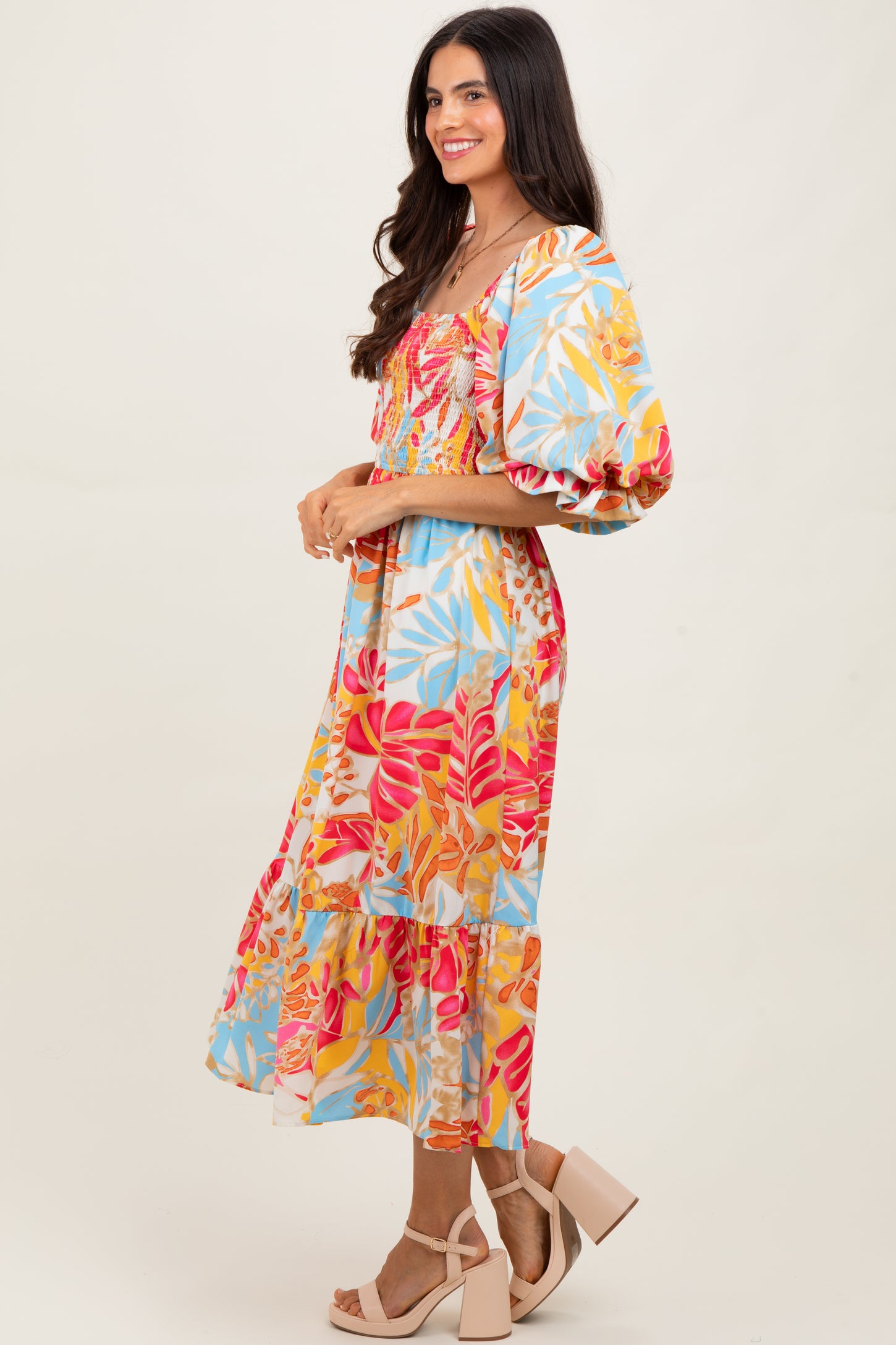 woman wearing a colorful floral midi dress with puff sleeves and a tiered skirt, paired with block-heeled sandals
