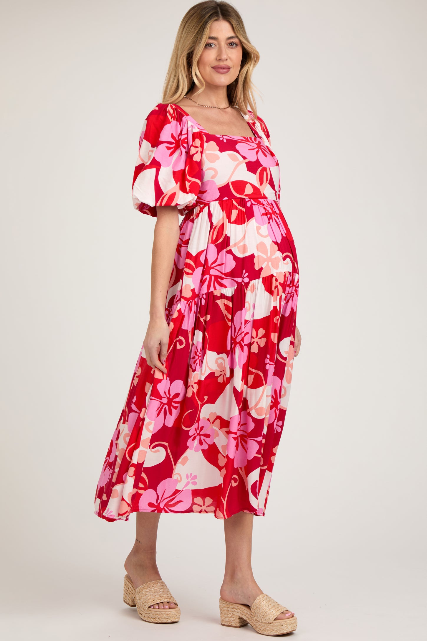 woman wearing a floral red maternity dress with puffy sleeves and a flowing skirt, showing her baby bump