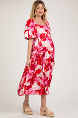woman wearing a floral red maternity dress with puffy sleeves and a flowing skirt, showing her baby bump