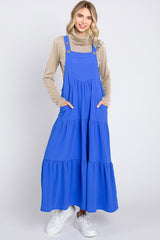 woman wearing a long blue tiered maxi dress with pockets and adjustable straps, styled with a beige turtleneck and white sneakers