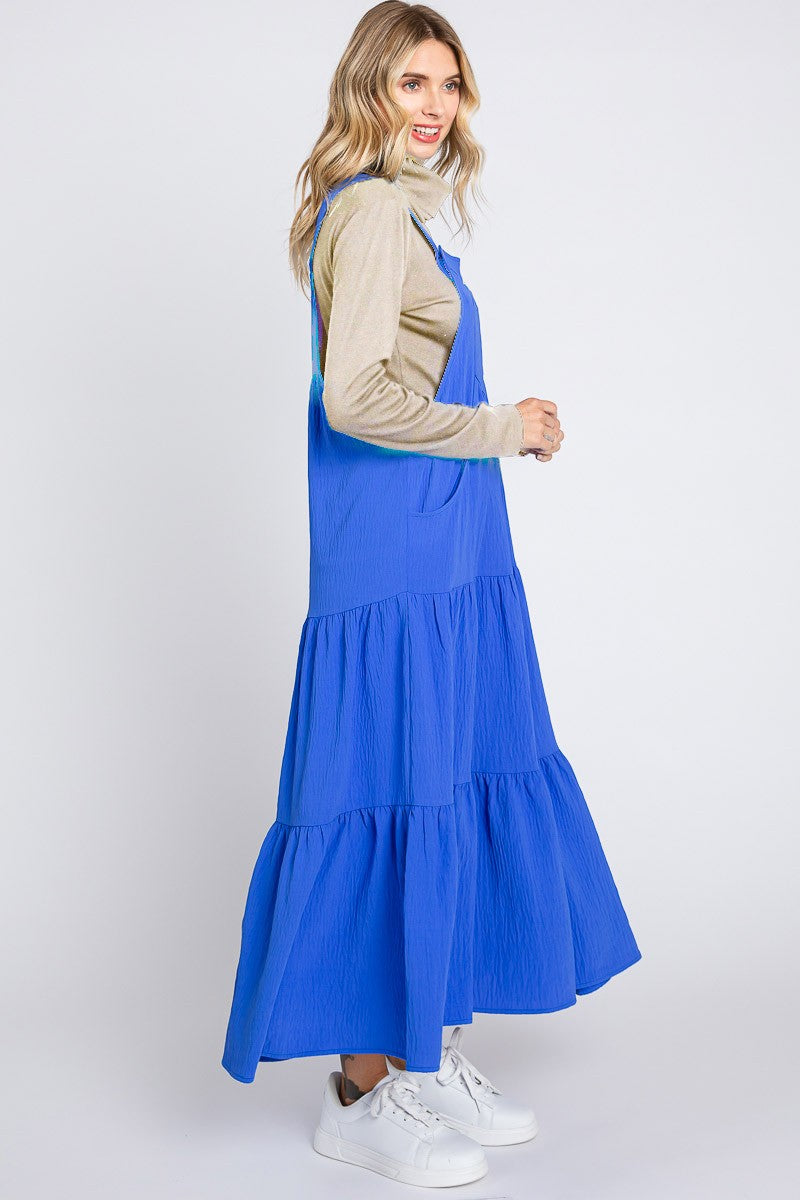 woman wearing a bright blue tiered maxi dress over a beige long sleeve top and white sneakers