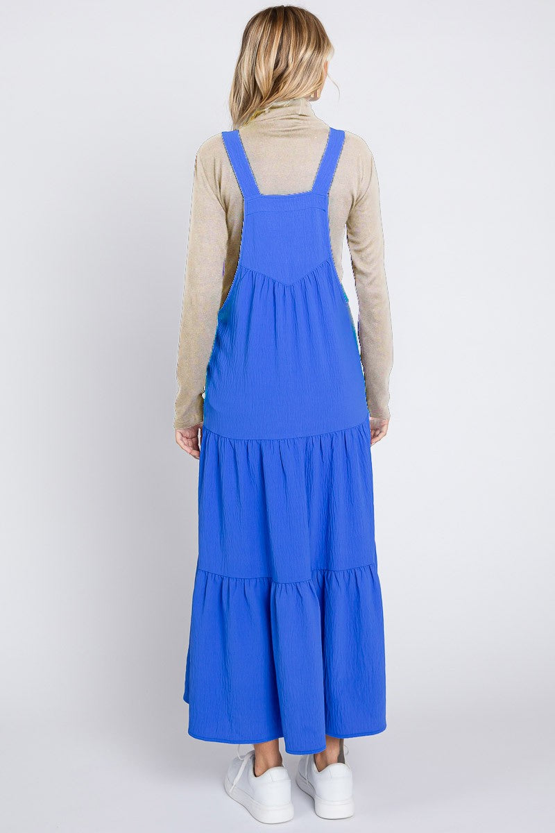 woman wearing a blue tiered maxi dress with adjustable straps and a beige long sleeve top underneath