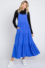 woman wearing a bright blue tiered maxi dress with pockets and side buttons, paired with a black long sleeve top and white sneakers