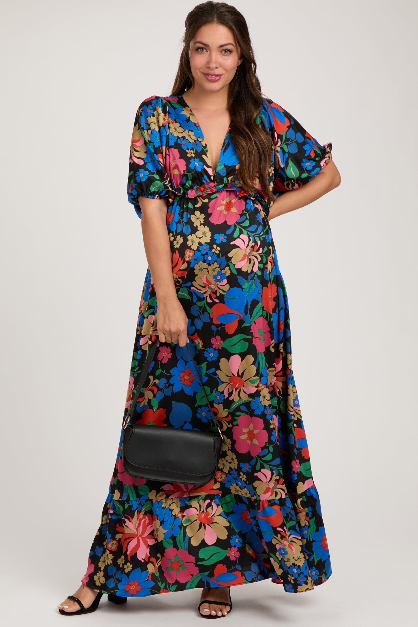 woman wearing a vibrant floral print maternity maxi dress with short sleeves and holding a black handbag, baby bump visible
