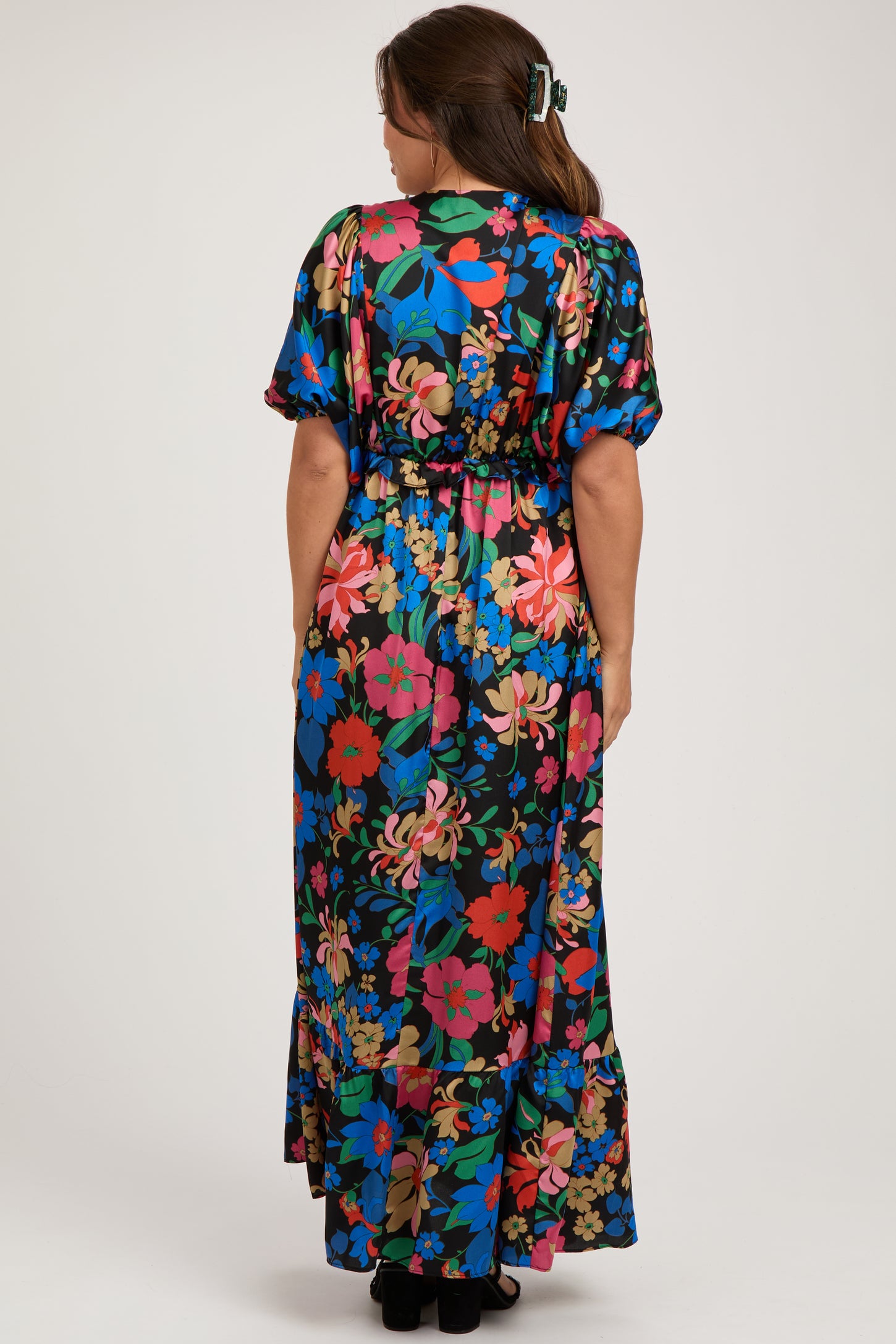 woman wearing a colorful floral maternity maxi dress with a cinched waist and short sleeves, facing away from the camera