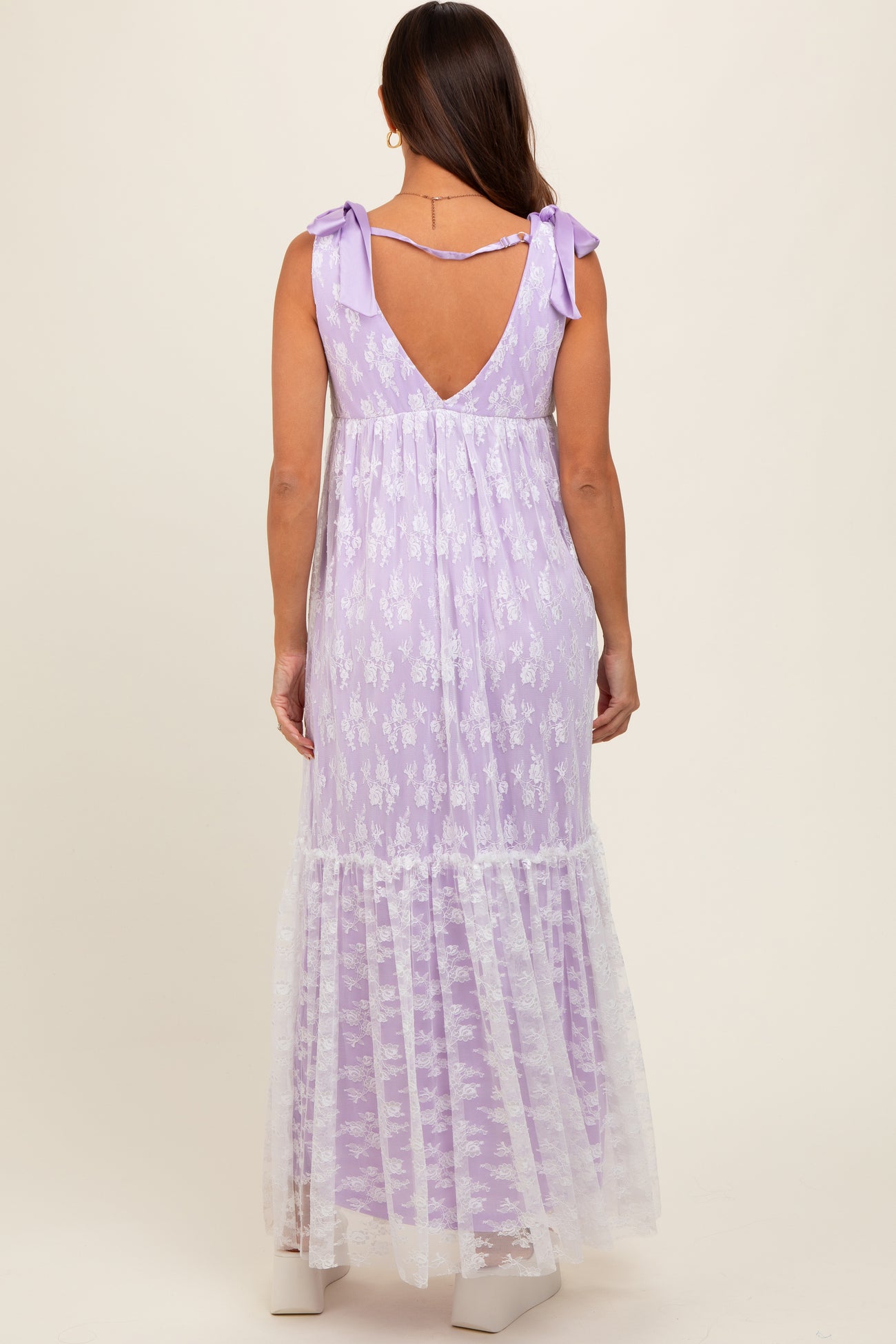 woman wearing a lavender maternity maxi dress with a lace hem and bow straps, showing her back