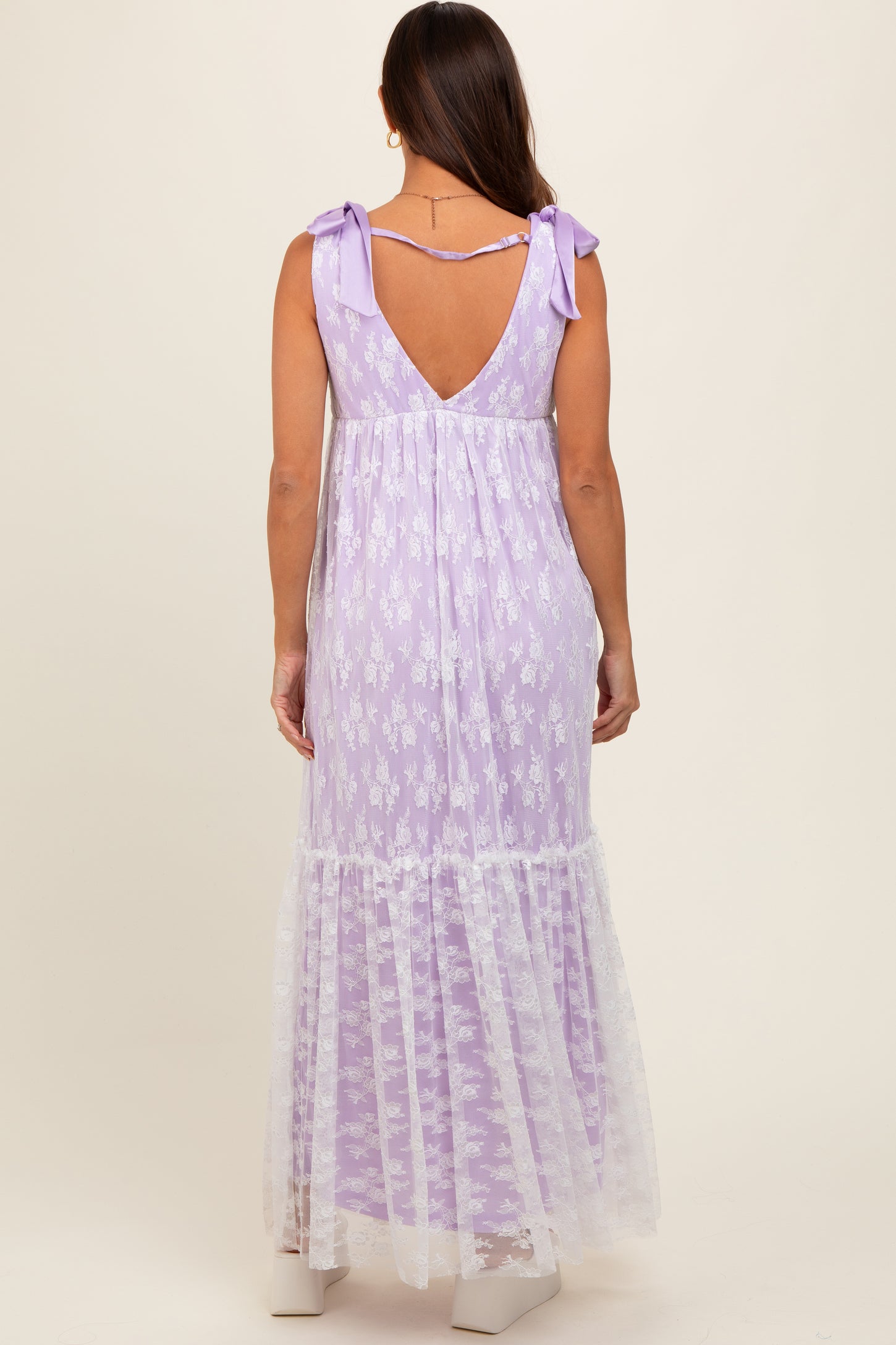 woman wearing a lavender maternity maxi dress with a lace hem and bow straps, showing her back