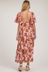 woman wearing a brown and pink floral maternity maxi dress with flutter sleeves and an open back, showing her baby bump