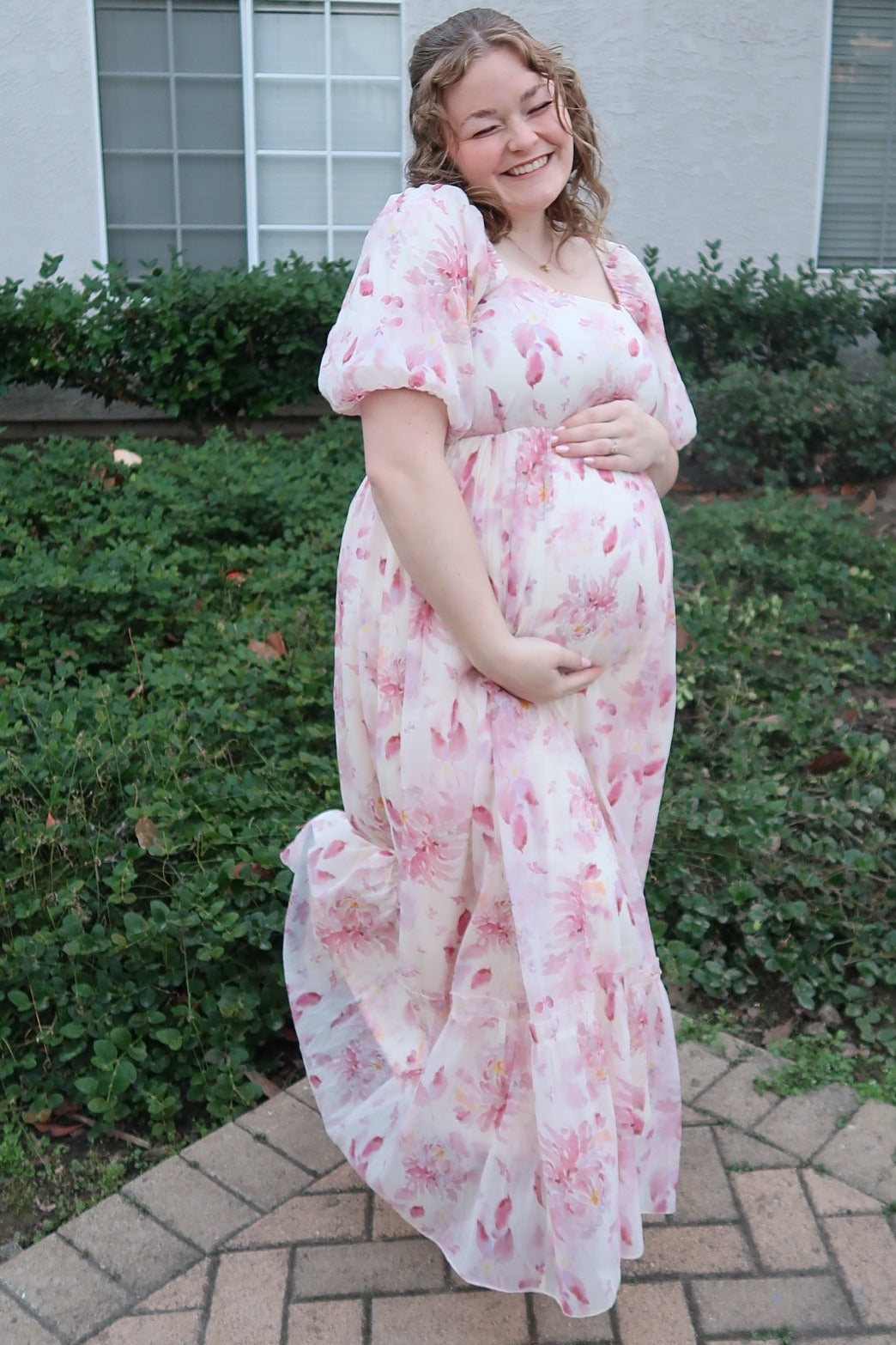 woman wearing a pink floral maternity maxi dress and holding her baby bump