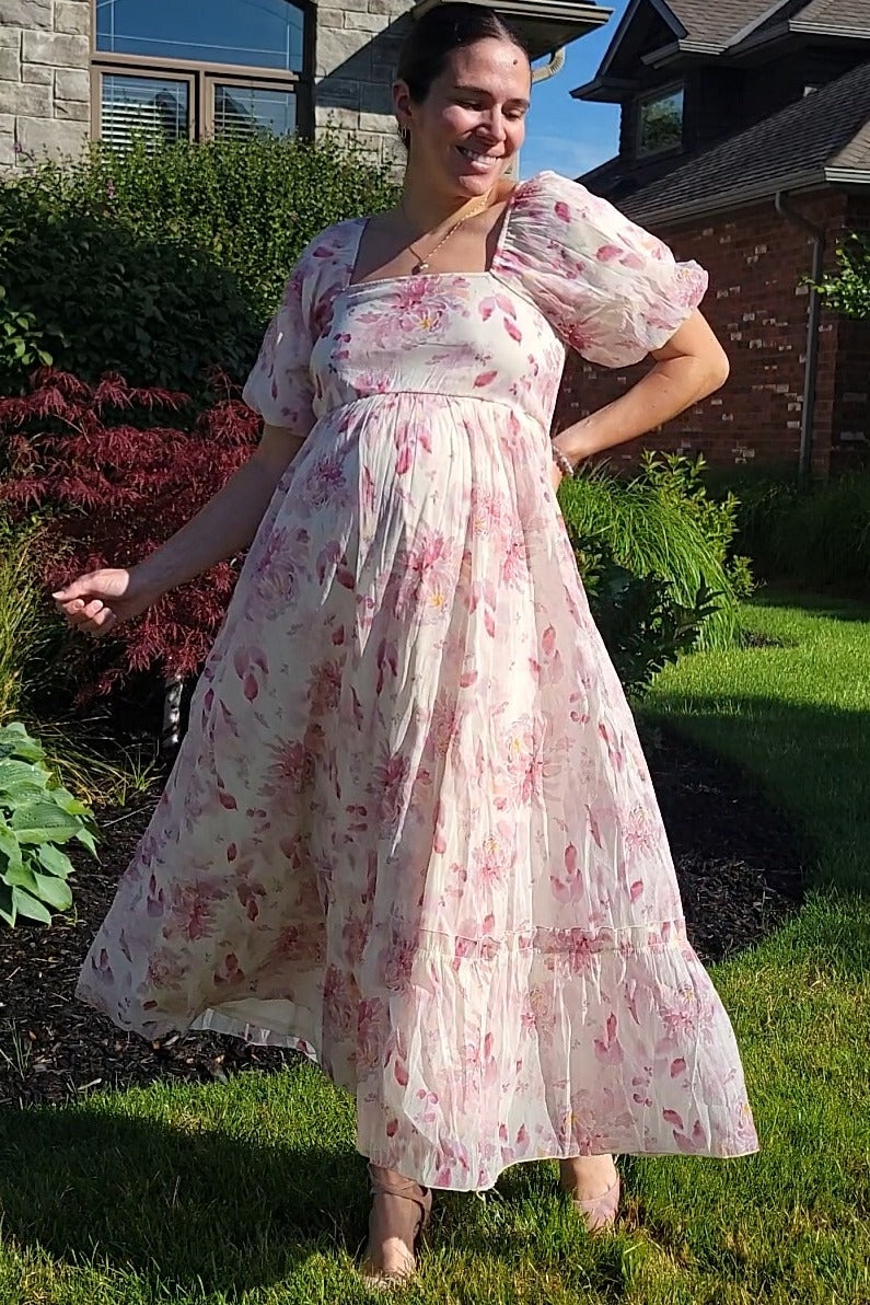 woman wearing a floral maternity dress with short puff sleeves and a flowing skirt, showing her baby bump outdoors