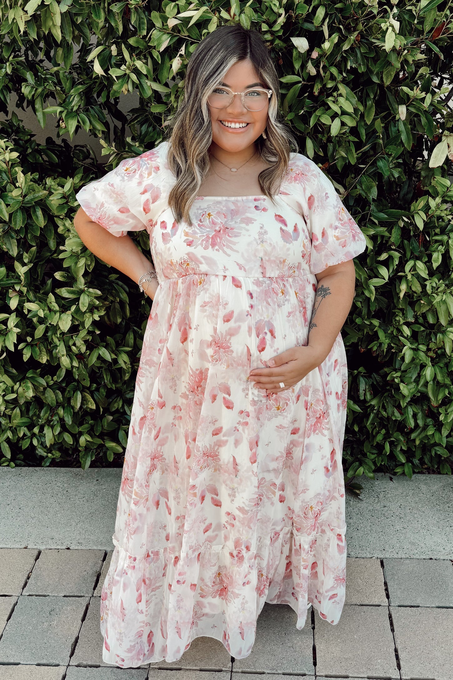 woman wearing a floral short sleeve maternity maxi dress with a visible baby bump, posing outdoors