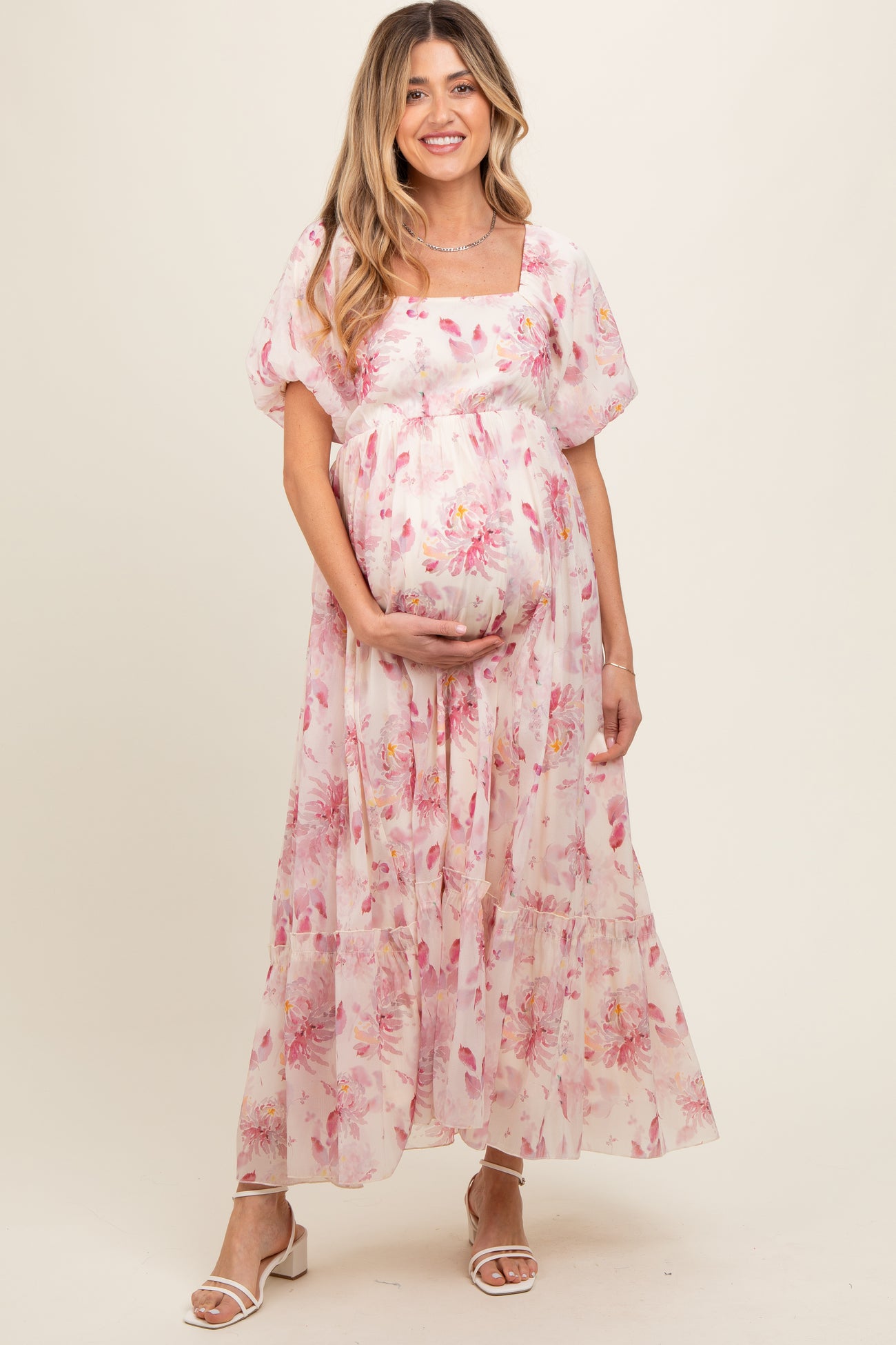woman wearing a pink floral maternity maxi dress, holding her baby bump, with puff sleeves and a square neckline