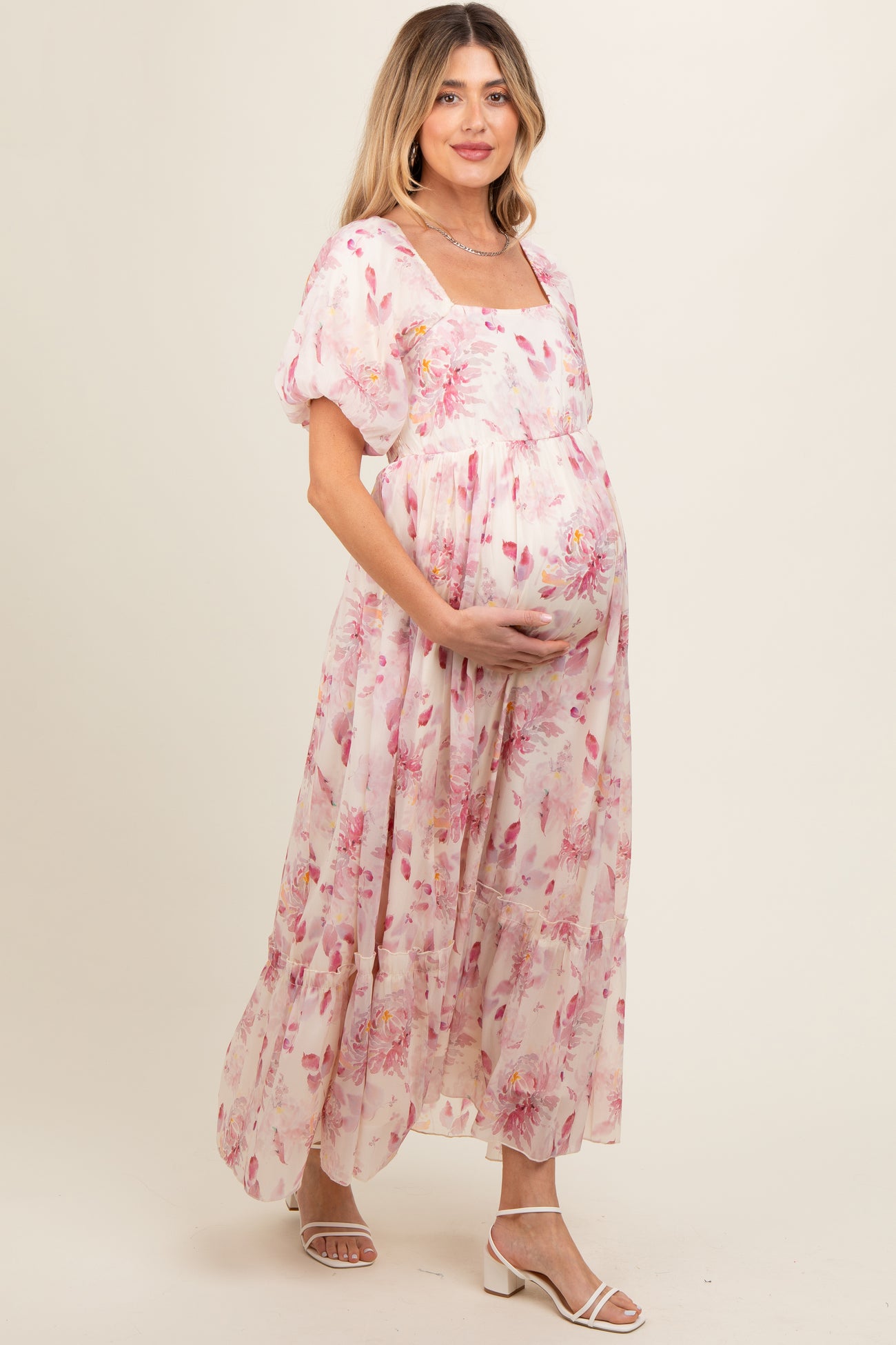 woman wearing a floral pink maternity maxi dress with puff sleeves and holding her baby bump