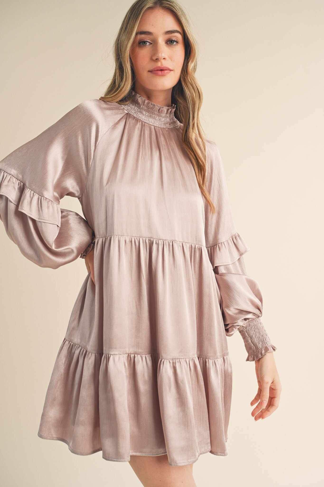 woman wearing a light pink satin tiered mini dress with ruffled sleeves and a high neckline
