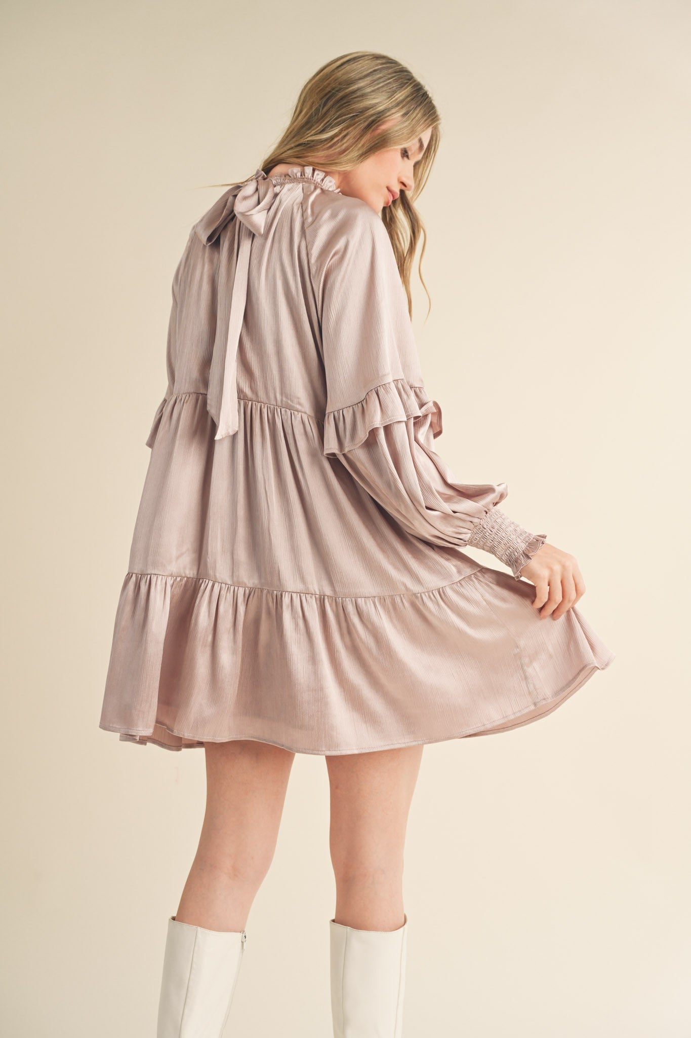 woman wearing a blush pink long sleeve tiered dress with ruffle details and a bow tie back