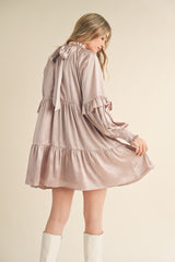 woman wearing a blush pink long sleeve tiered dress with ruffle details and a bow tie back