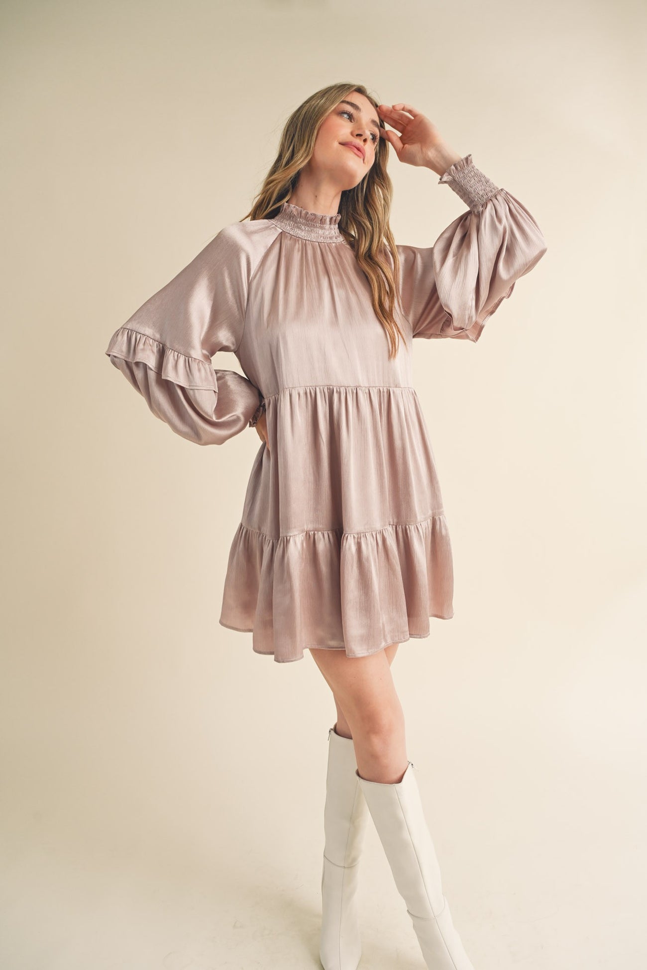 woman wearing a light mauve long sleeve dress with a tiered hemline and ruffled sleeves standing against a neutral background