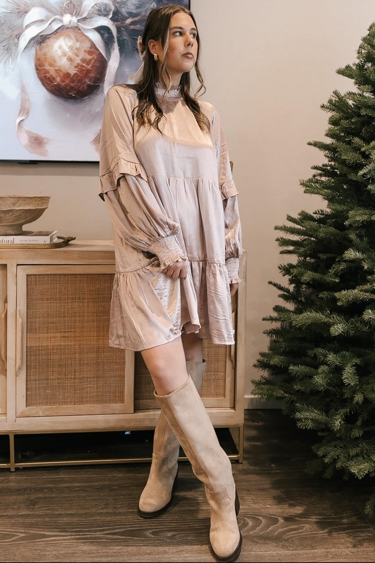 woman wearing a light pink tiered mini dress with ruffle details and knee-high beige boots