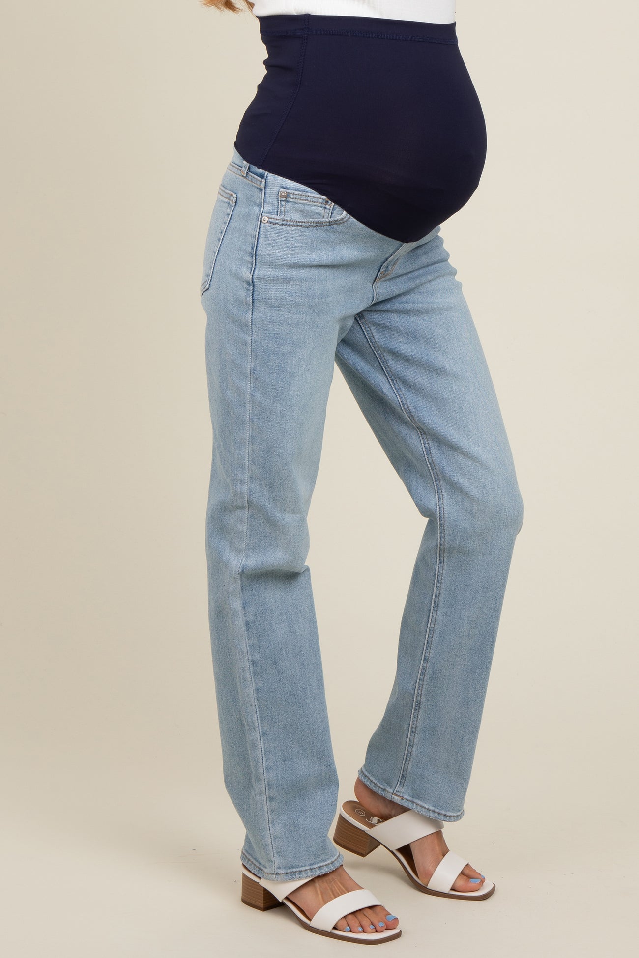 woman wearing light wash maternity jeans with a navy blue over-the-bump panel and a visible baby bump