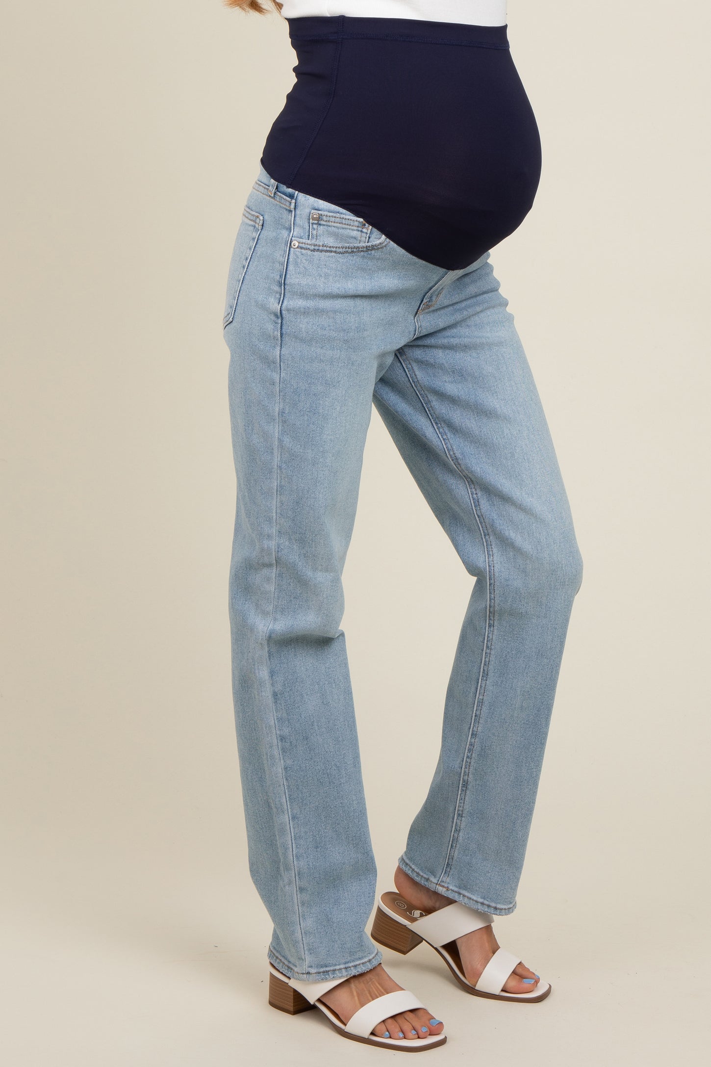 woman wearing light wash maternity jeans with a navy blue over-the-bump panel and a visible baby bump