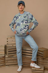 woman wearing a floral patterned light blue maternity sweater and light blue jeans, posing with a baby bump visible