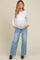 woman wearing a white long sleeve maternity top and light blue wide-leg jeans, showing her baby bump