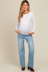 woman wearing a white long sleeve maternity top and light blue jeans, showing her baby bump