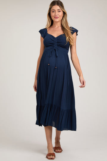 woman wearing a navy blue maternity dress with short sleeves and a gathered bust, showing off her baby bump