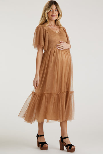 woman wearing a brown maternity dress with short puff sleeves and a tiered tulle skirt, showing her baby bump