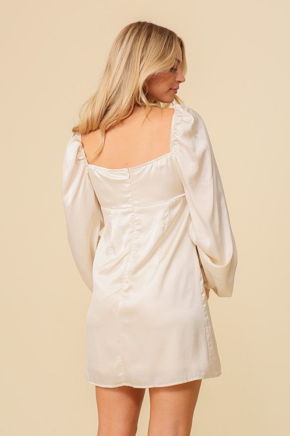 woman wearing a cream short dress with puff sleeves and a square neckline, showing the back view