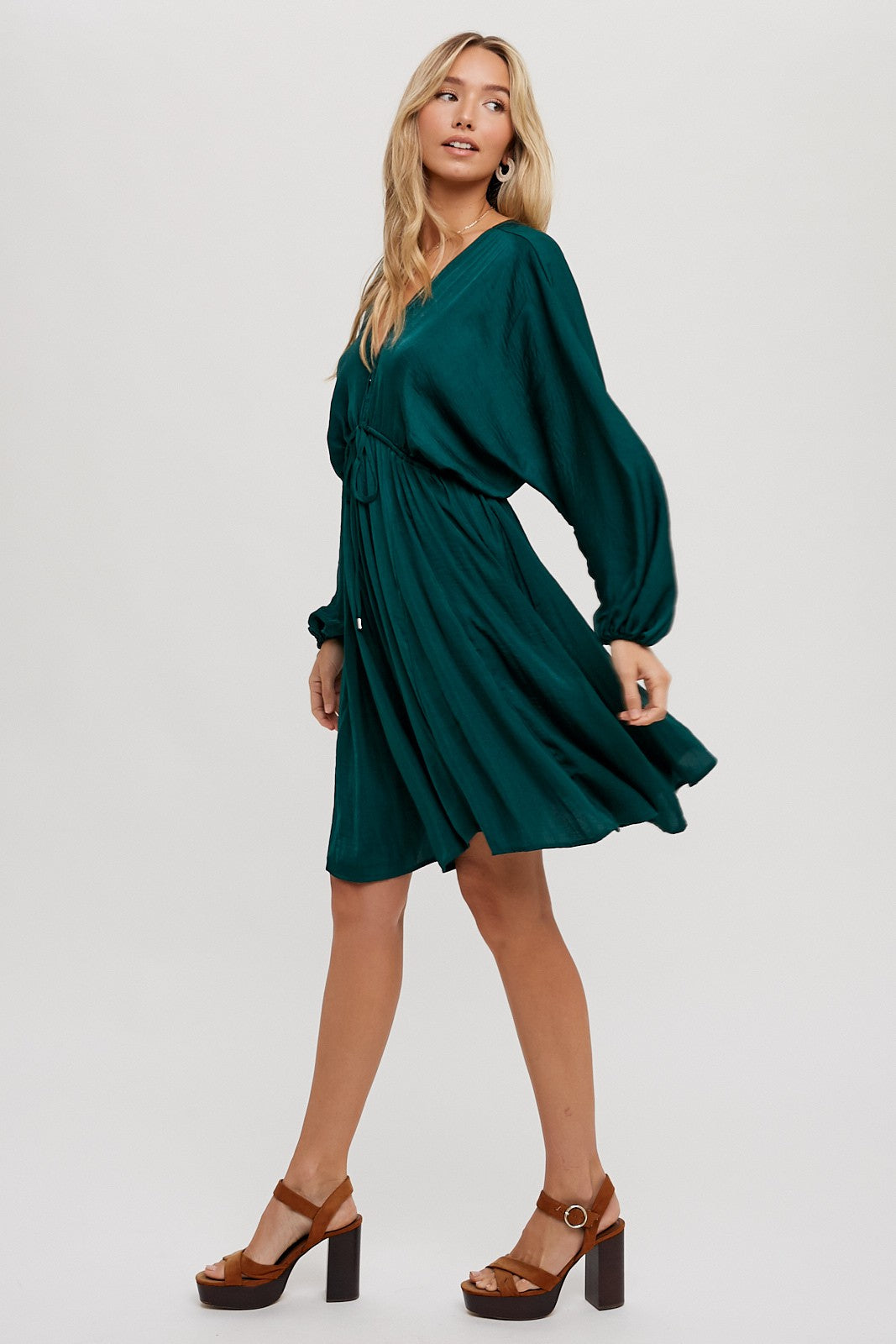 woman wearing a teal short sleeve dress with a cinched waist and flowing skirt, paired with brown block heeled shoes