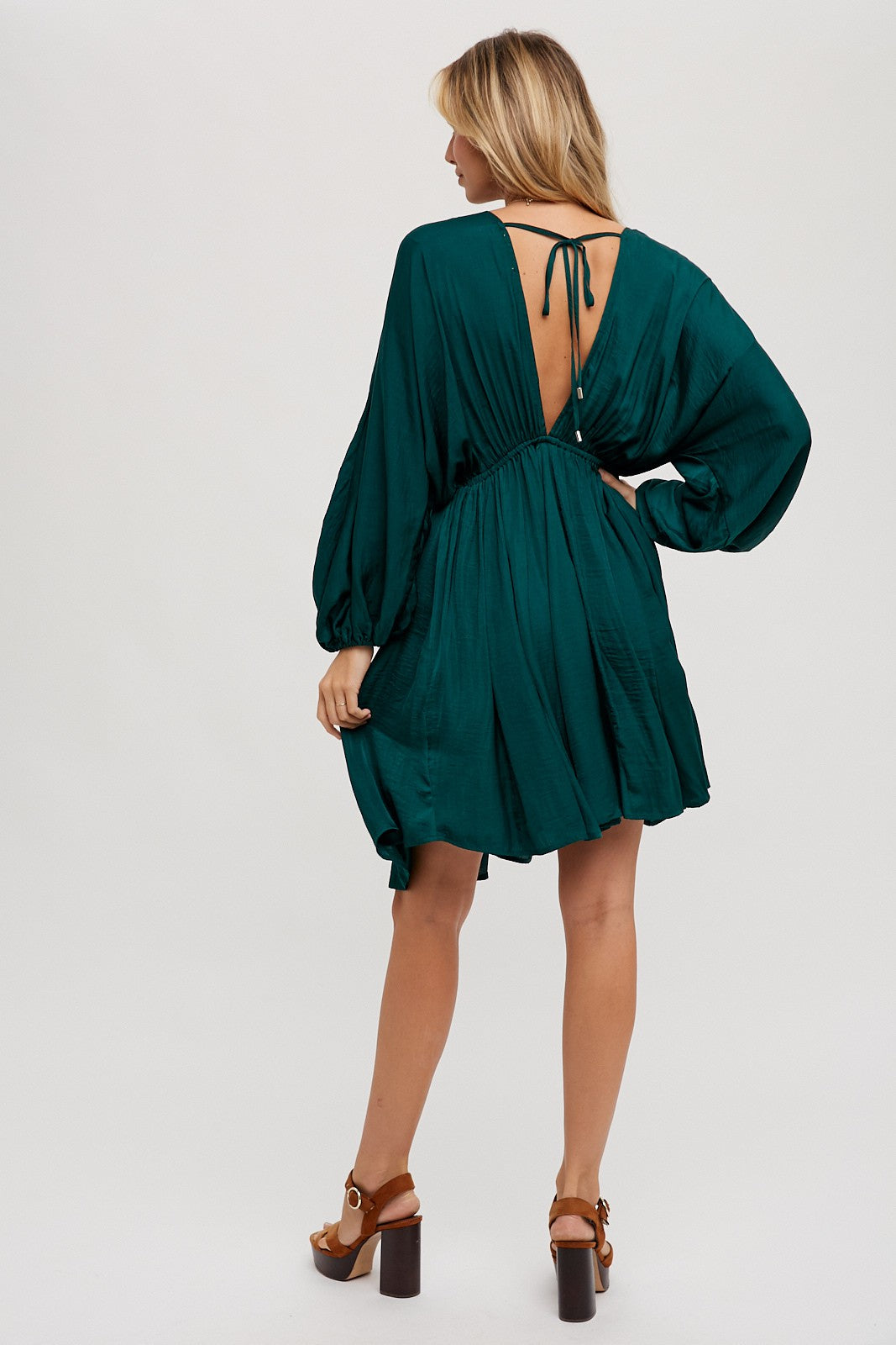 woman wearing a teal short dress with a deep back neckline and puff sleeves, showing a stylish and elegant look