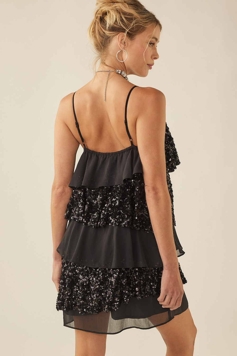 woman wearing a black sequin tiered mini dress with thin straps and an open back