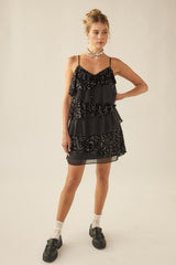 woman wearing a black tiered sequin dress with thin straps and chunky black loafers, standing with a confident pose