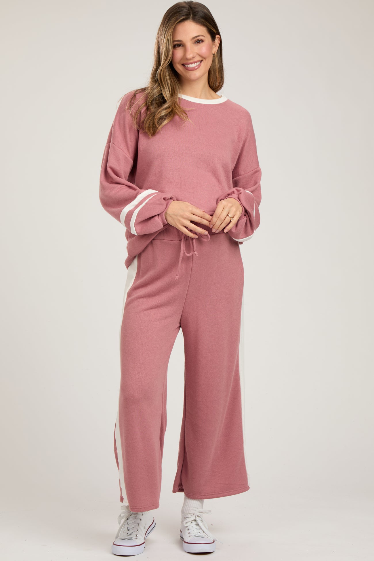 woman wearing a pink maternity sweater and matching wide-leg pants, holding her baby bump