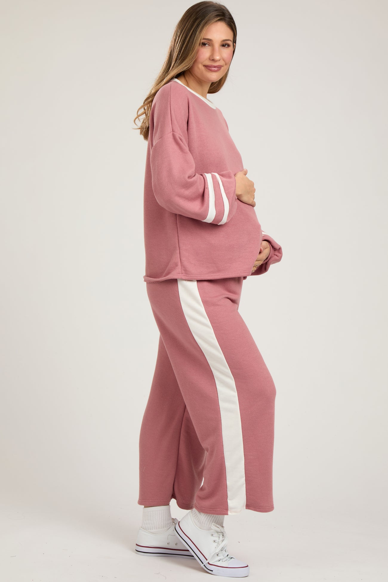 woman wearing a pink maternity loungewear set with white stripe details, holding her baby bump