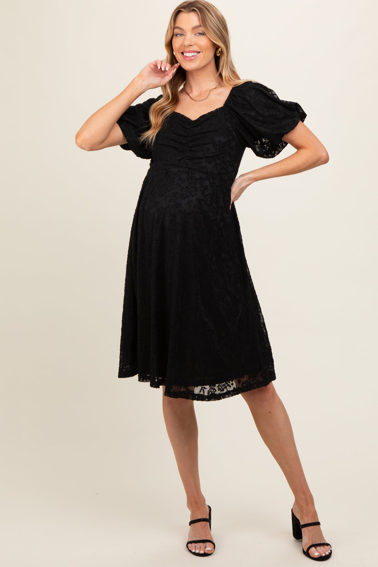 woman wearing a black short sleeve lace maternity dress with puffed sleeves and a fitted bodice, showing her baby bump